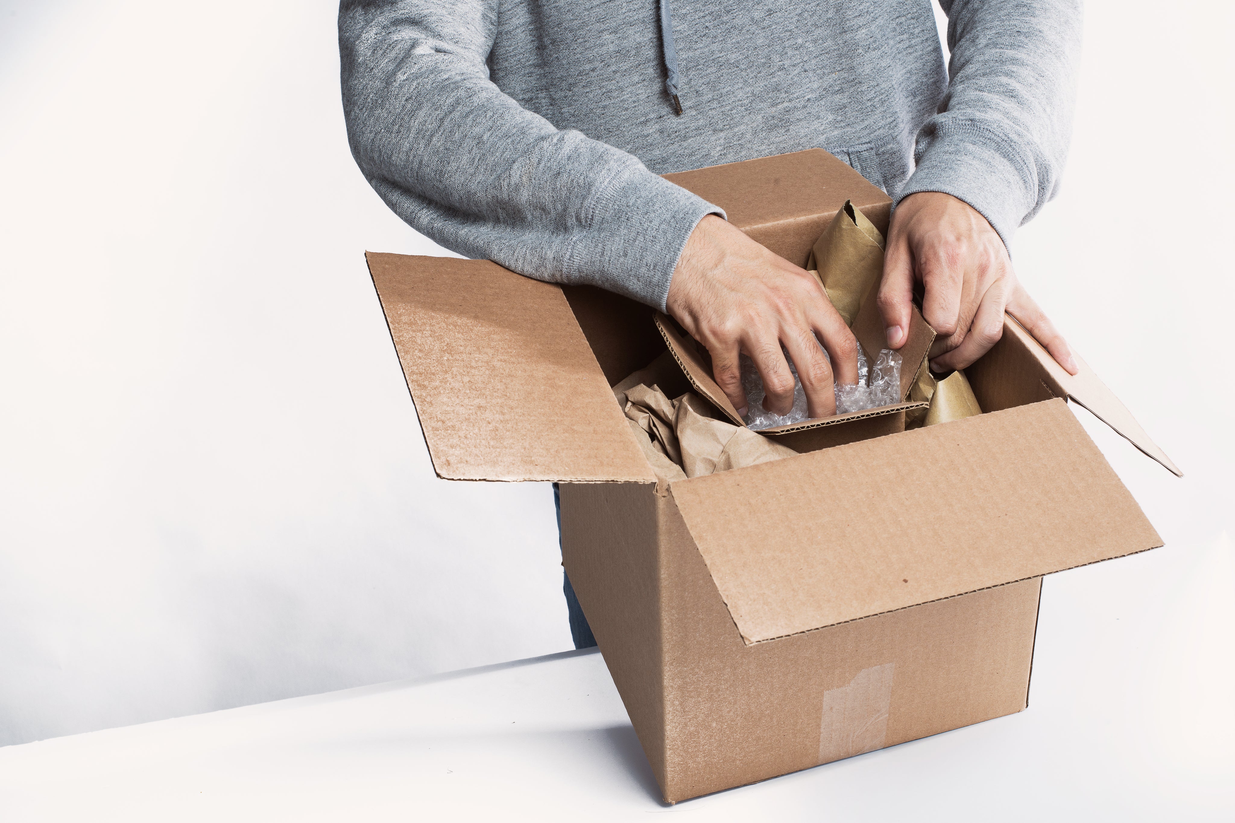 Mensch, der gerade etwas in einen Karton verpackt. In dem Karton ist ein zweiter Karton zusammen mit Füllmaterial.